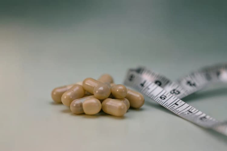 Os suplementos para emagrecer são realmente eficazes? Close-up de cápsulas de suplementos com um medidor de fita métrica ao lado